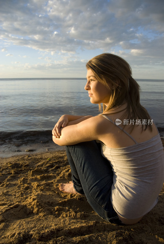 一个年轻的女人坐在海滩上，看起来若有所思