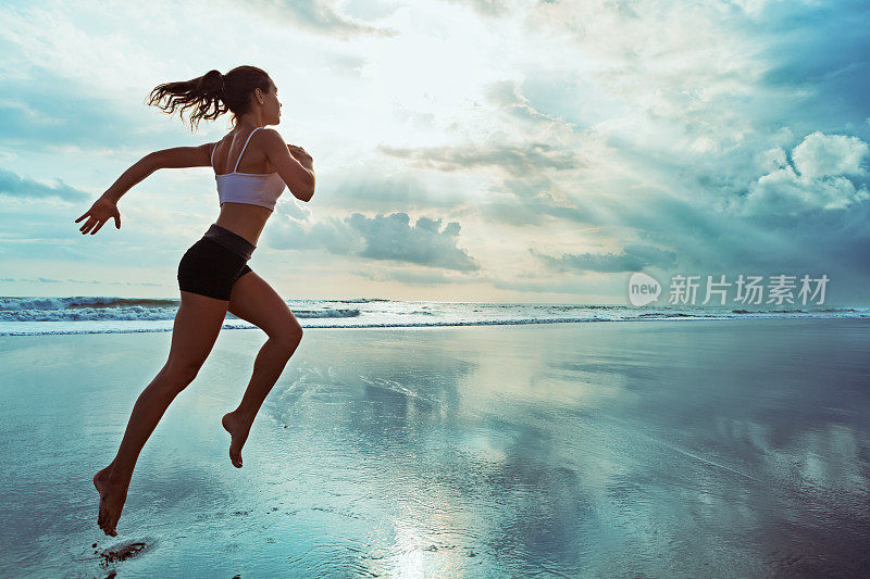 活跃的运动女人沿着日落的海洋海滩跑步。运动背景。