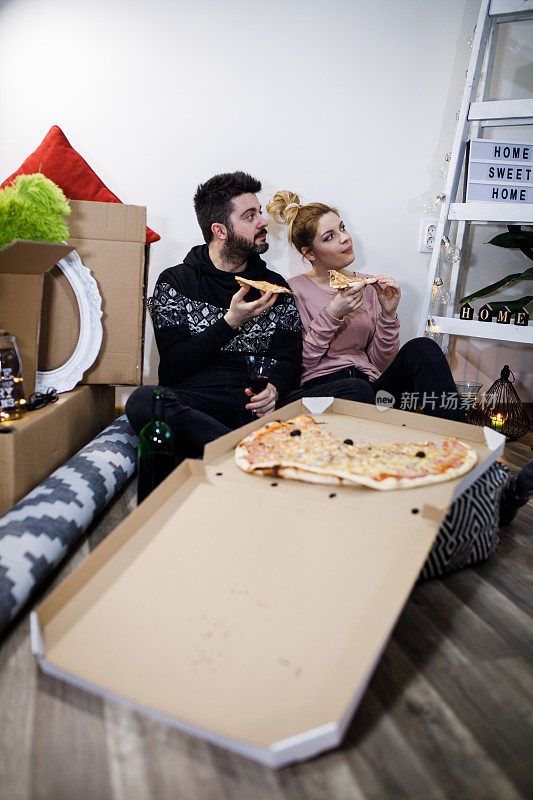 快乐的年轻夫妇有一个披萨午餐休息地板后，搬进了一个新的家与周围的盒子