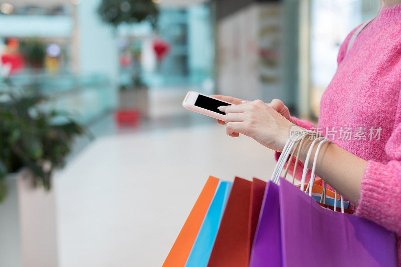 在商场里拿着购物袋用智能手机的女人