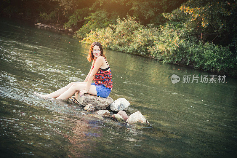 女孩坐在河里的一块石头上
