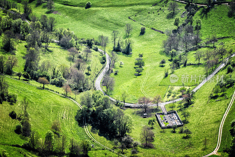 鸟瞰图，法国乡村小墓地，周围的绿色草地在春天，与曲折的Bugey山路在Ain部
