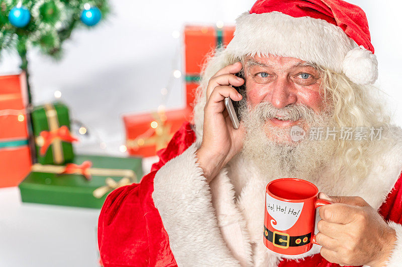 圣诞老人对着镜头微笑，手里拿着智能手机