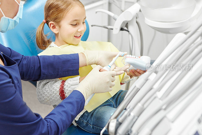 牙医教一个小女孩如何正确刷牙，并示范一个模型。