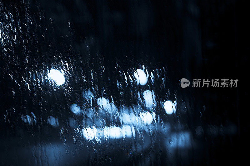 抽象的雨滴落在窗户上，模糊了城市的灯光