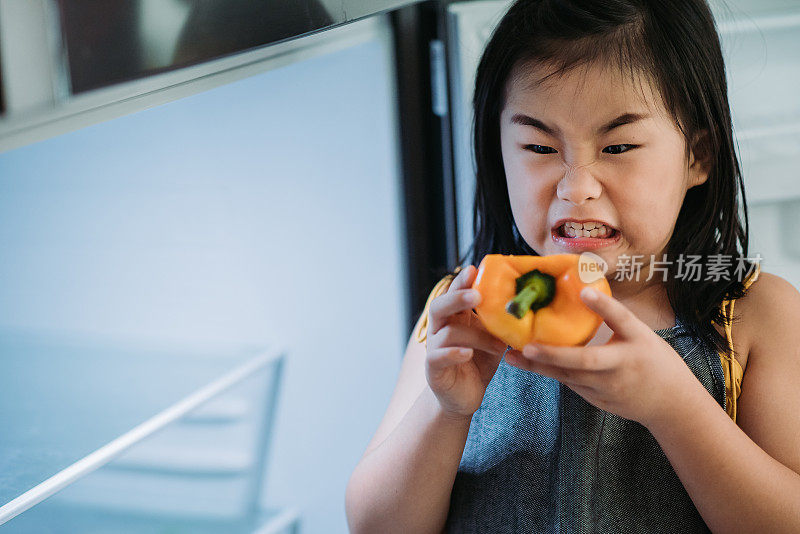 亚洲华人女性儿童手握甜黄甜椒与她的愤怒表情前冰箱在厨房