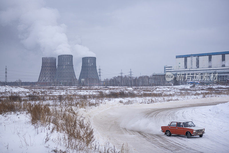 俄罗斯一辆红色的老车瓦兹日古里正在漂移中飞快地行驶，在公路的背景下，一个热电站在冬天的雪地里。