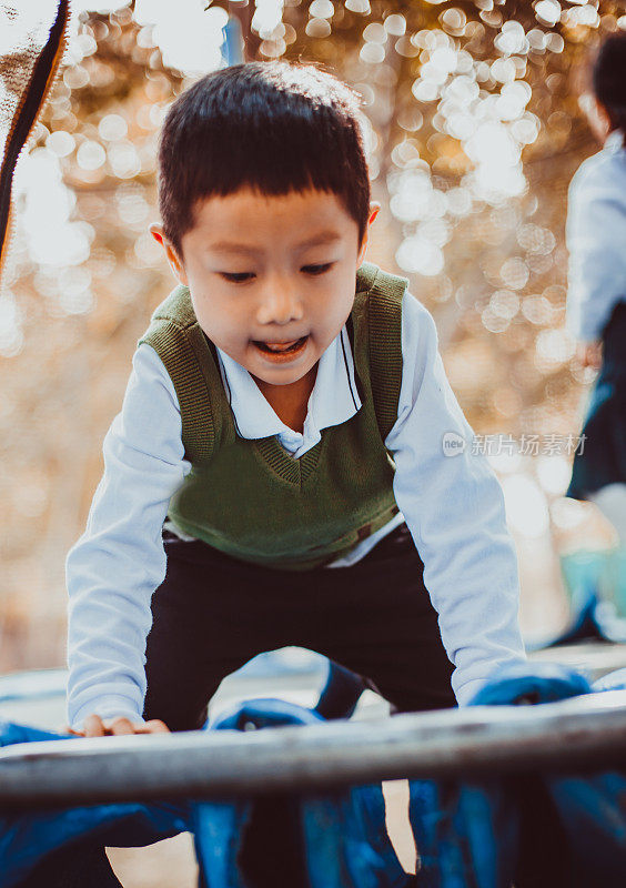 可爱的亚洲幼童有乐趣尝试爬上一个方格架