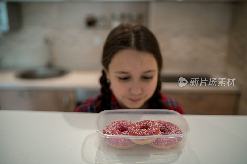 对孩子的饮食。悲伤和不快乐的孩子触及甜甜圈。孩子们的美味食物。孩子在看甜甜圈。垃圾食品上瘾。