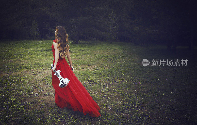 穿着红衣服的小提琴家正在森林里的草地上走着