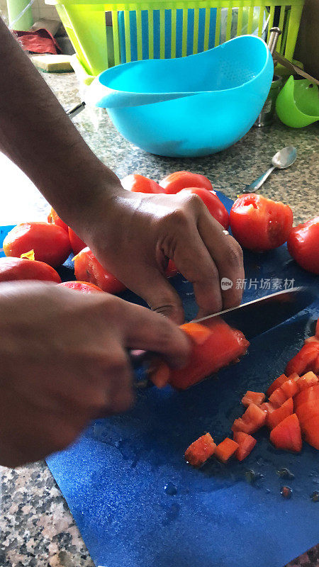 一个不认识的男人在家庭厨房的菜板上切着番茄，一个男人拿着锋利的刀切着番茄，切碎的番茄用来做意大利面酱，戴着手镯