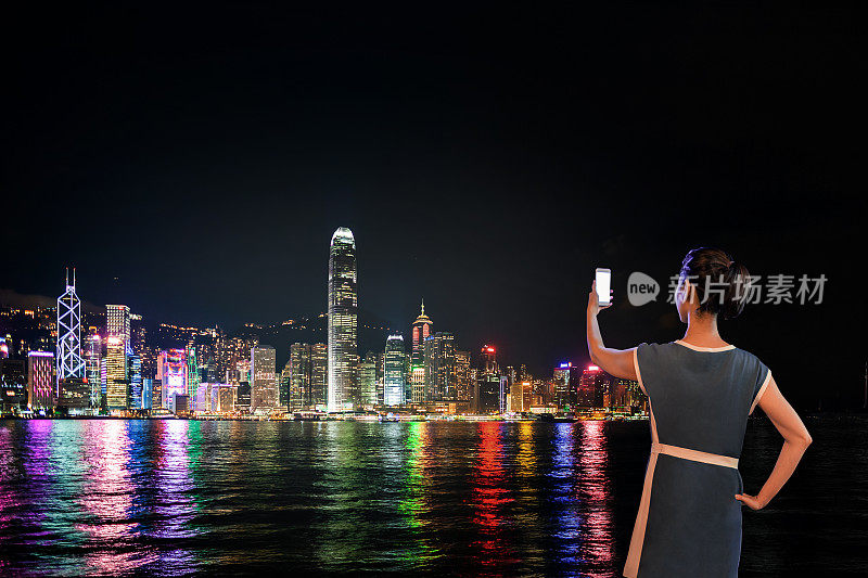一名中国妇女晚上在香港维多利亚港使用手机