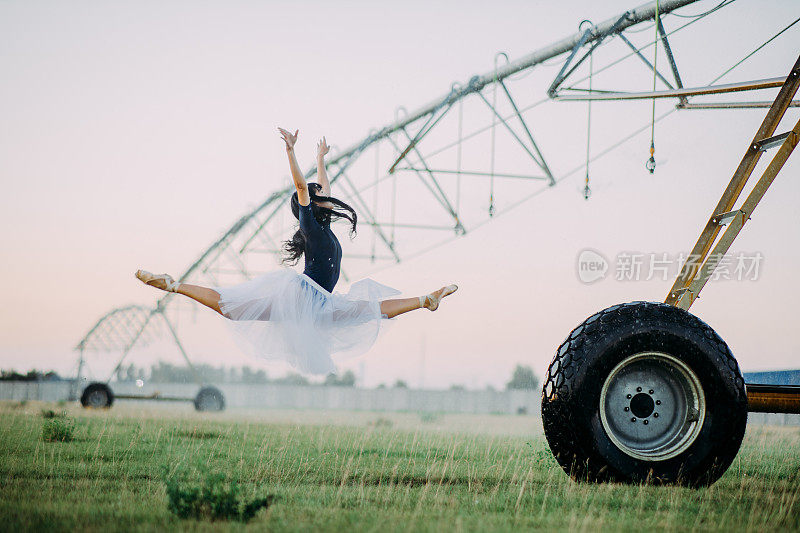 芭蕾舞演员在农用喷雾器附近的农场上跳跃和表演体操。