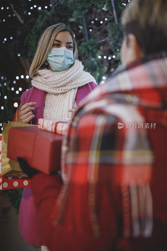 年轻女子在保护面罩和她的母亲交换圣诞礼物