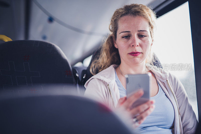 年轻漂亮的女人在公共汽车上使用手机。