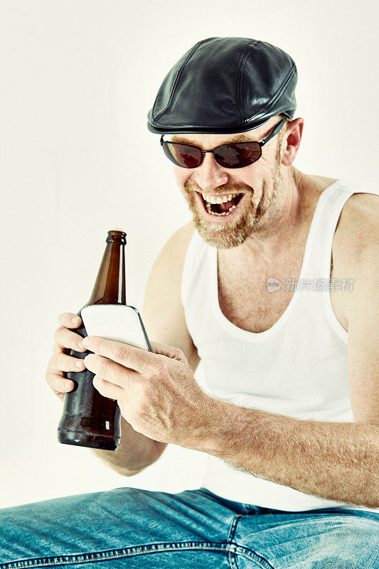身穿汗衫的中年男子拿着啤酒瓶，一边拿着手机一边笑