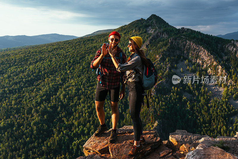 一对幸福的夫妇在山上欣赏美丽的景色。一男一女背着背包在山上欣赏全景。旅行者喜欢在日落时爬山。本空间