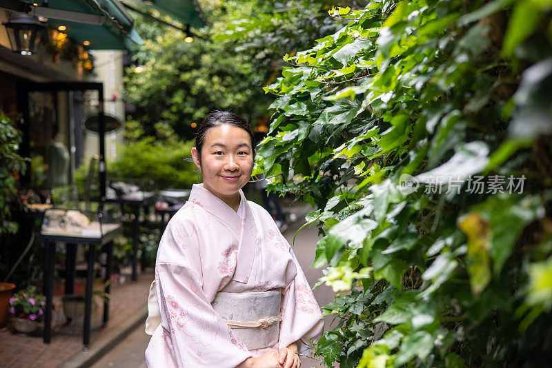 一名日本妇女站在铺满绿叶的狭窄街道上的肖像