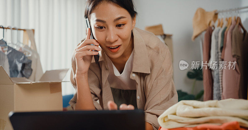 年轻的亚洲小企业主女性使用手机接收订单，并在家里用平板电脑检查库存。