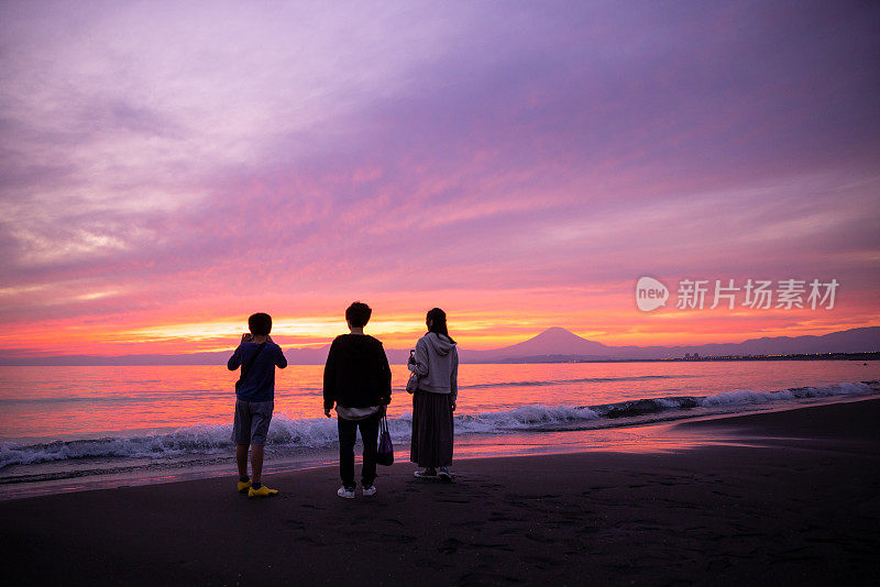 夕阳西下时，三个人从湘南海滩看富士山的后视图