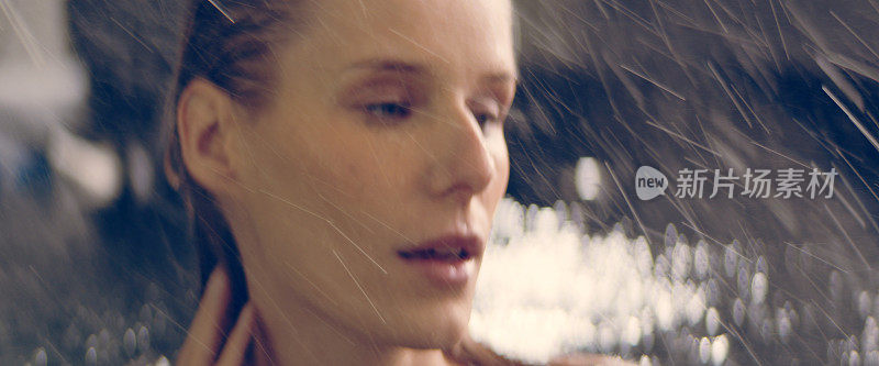 自然的女人从水里冒出来，享受着雨。轻轻地抚摸着她的脸和长发。美容护理的比喻