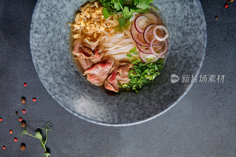 越南菜-牛肉米粉面汤或米粉汤。与新鲜的绿色蔬菜在蓝色碗上纹理深灰色的桌子。麻辣肉汤。前视图。
