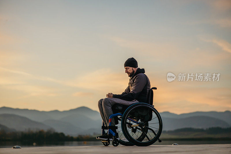日落时分，一名残疾人坐在轮椅上，在码头上用手机发短信