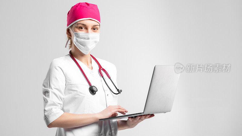 职业医生在工作室的女性肖像。为远程医疗使用笔记本电脑的妇女。孤立背景下的概念。妇女使用口罩进行冠状病毒卫生保健