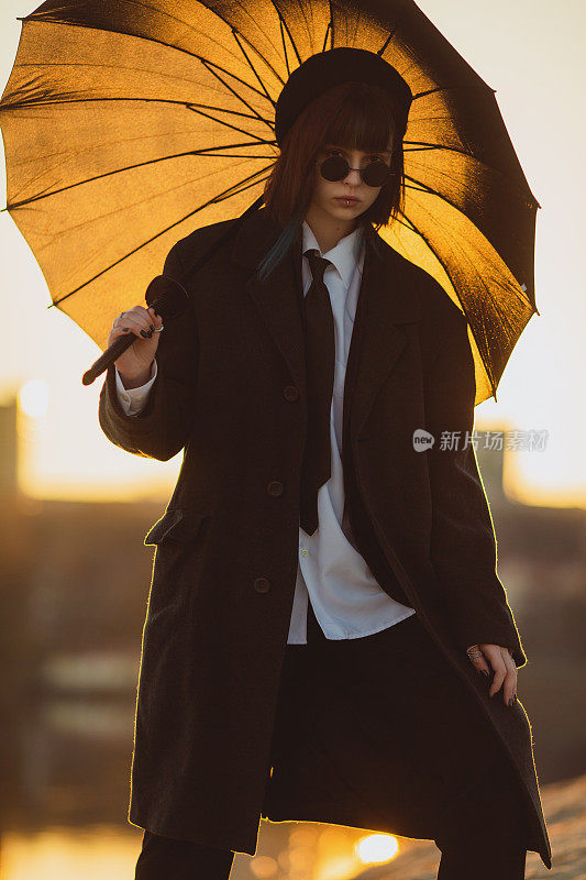 红发女孩在日落背景下的户外。哥特式风格。亚洲时尚模特，黑色外套，雨伞，自然。黑色的太阳镜。时尚的衣服。青年现代风格。亚文化