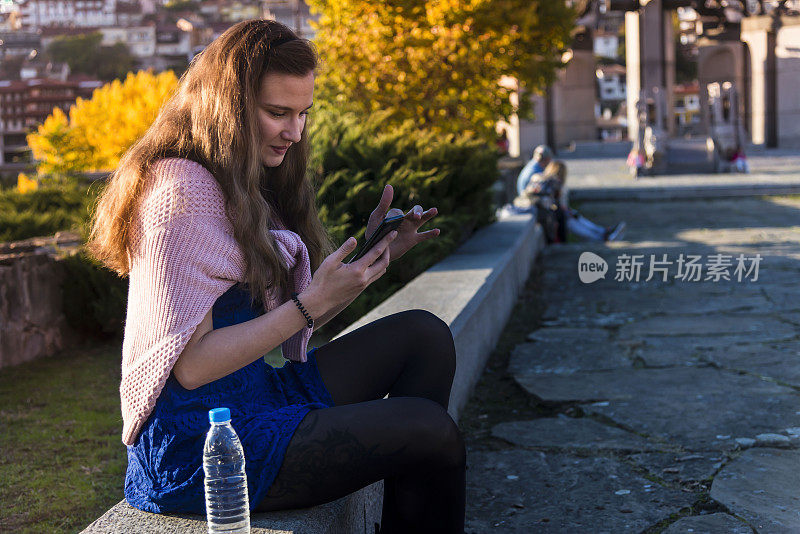 年轻的时髦女人在日落时使用智能手机