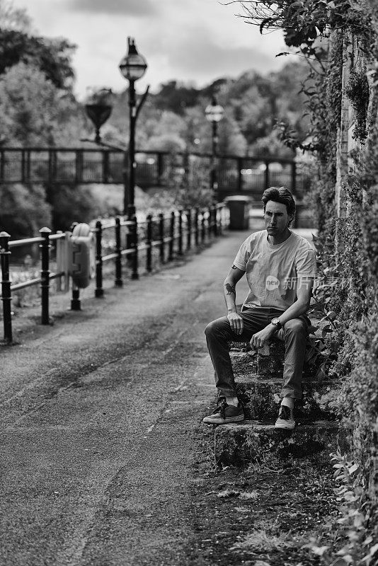 一个30多岁的男人坐在桥旁的旧台阶上