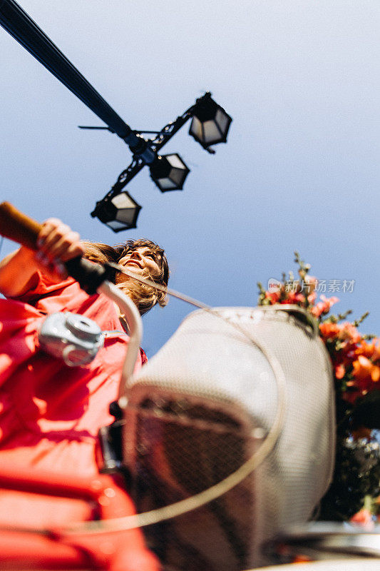 开朗的女人骑着她的复古自行车，Instax相机以蓝天为背景