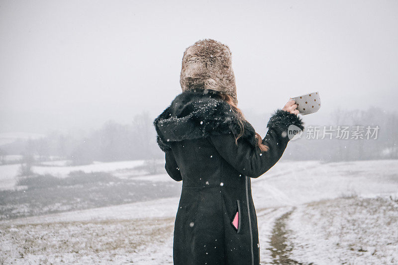 站在雪地上拿着一杯茶的年轻女子