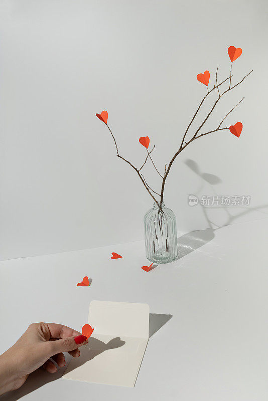 树枝上有红纸做的心形，女性的手把心形放在白色的信封里。最小限度的爱或情人的概念。