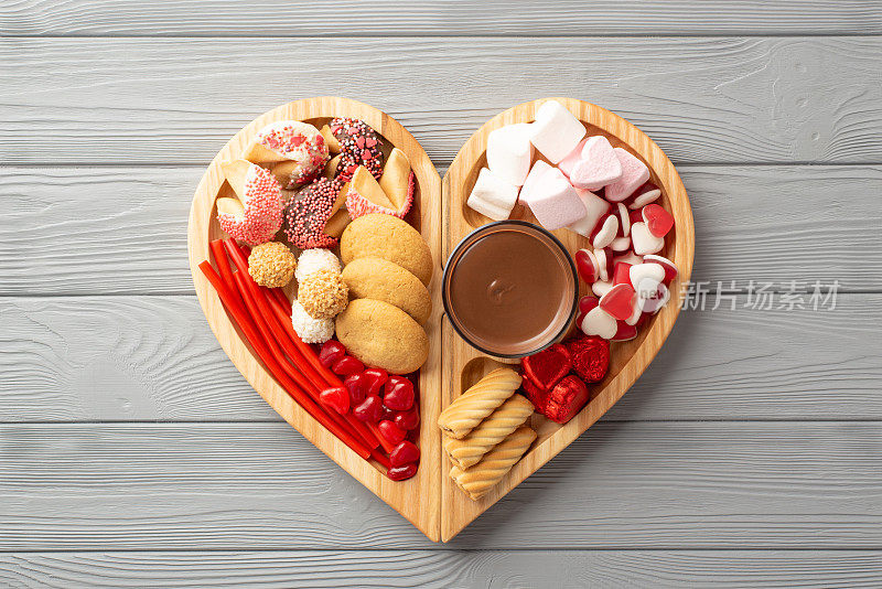 情人节的概念。顶部视图照片的木制心形托盘与糖果饼干和玻璃杯的热巧克力在灰色的木桌背景