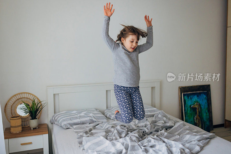 小女孩在明亮的卧室的床上跳得很开心。快乐童年概念