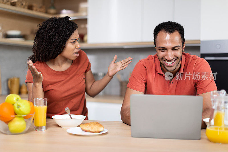失望愤怒的年轻非洲裔美国妻子尖叫微笑的丈夫，男人玩笔记本电脑