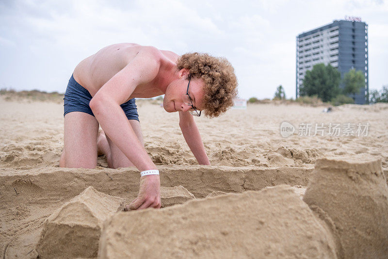 一个大男孩正在沙滩上堆沙堡。