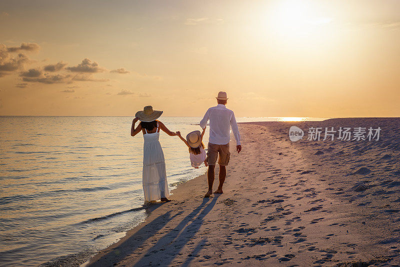 一个幸福的家庭在日落时手牵手走在天堂般的海滩上
