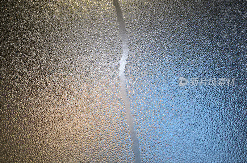 窗户玻璃上凝结有小水滴。冬天的季节。湿表面雾化玻璃。美丽的图案纹理自然光线照射。