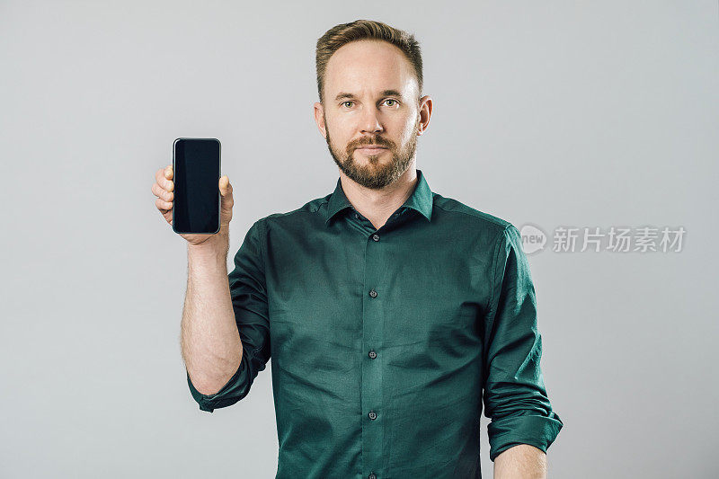 照片中，一个兴高采烈的英俊男子正在展示智能手机