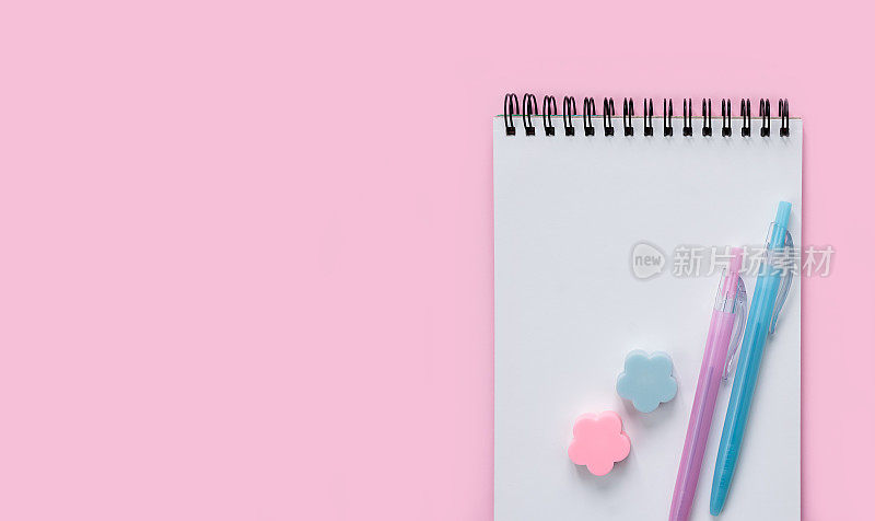空白记事本，彩色钢笔和橡皮在粉红色的背景。Flatlay。前视图。副本的空间。