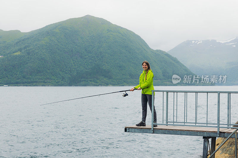 身穿绿夹克的女子在挪威峡湾钓鱼