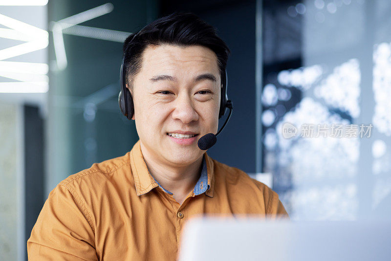 心情愉快的韩国人戴着耳机坐在电脑前的现代办公室里，在呼叫中心工作的亚洲人给客户提供咨询，敲击键盘