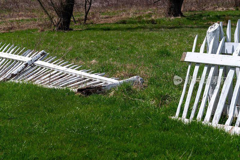白色的尖桩篱笆和腐烂的柱子躺在绿色的草地上