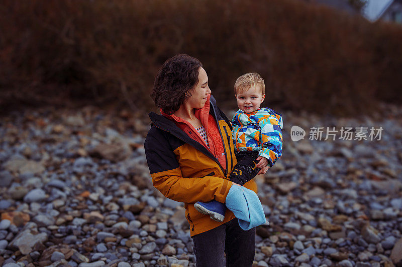 母亲抱着蹒跚学步的儿子站在岩石海岸线上