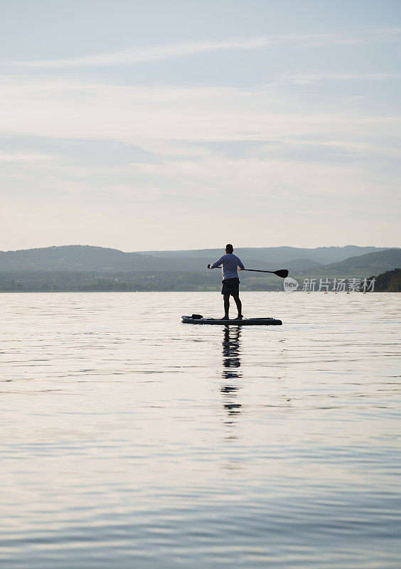 一名男子正在湖面上训练SUP板。站起来划桨。背景是风景。享受假期。积极的生活方式。一个男人的剪影。拿着桨。