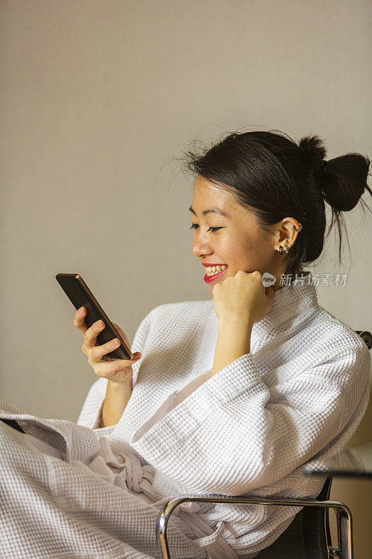 穿着长袍在室内使用手机的年轻亚洲妇女