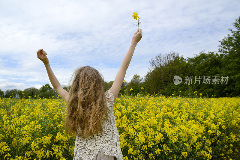 一个十几岁的女孩在油菜田里，手里拿着一朵花