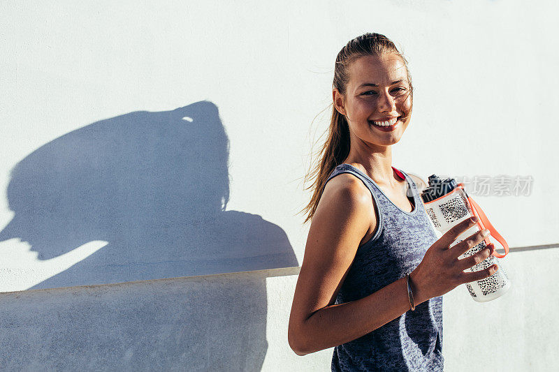 快乐的女跑步者拿着水瓶，微笑着